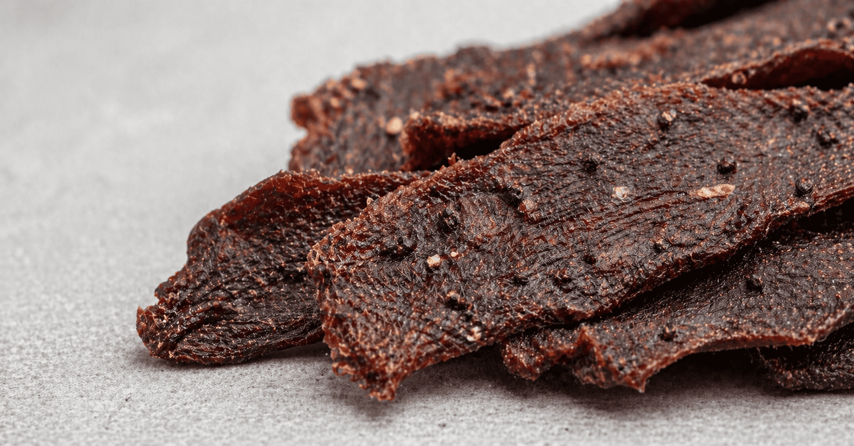 Close-up of dried beef jerky strips showing the fibrous texture and black pepper seasonings that can be harmful to pets.